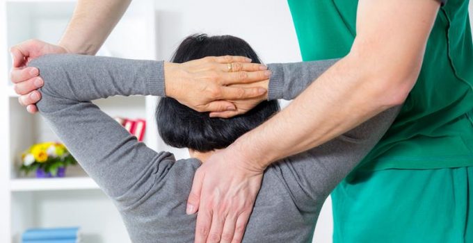 a man physician with a green shirt holding her left arm with one hand on top of the spine to stretch out muscles in Grand Rapids, MI