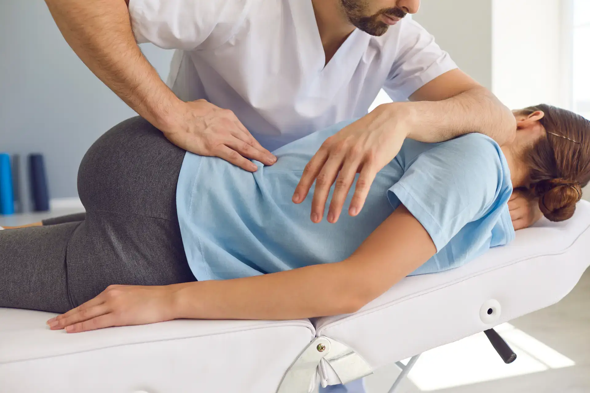 A chiropractor is performing a spinal adjustment on a patient who is lying face down on a treatment table in a clinic. This image could represent chiropractic care services available in Grand Rapids, MI.