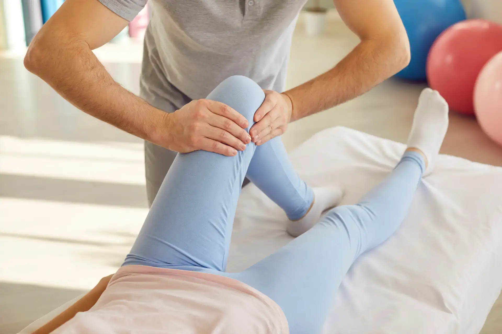 A physical therapist is examining a patient's bent knee while the patient lies on a treatment table, highlighting a hands-on assessment. This scene could represent physical therapy services offered in Grand Rapids, MI.