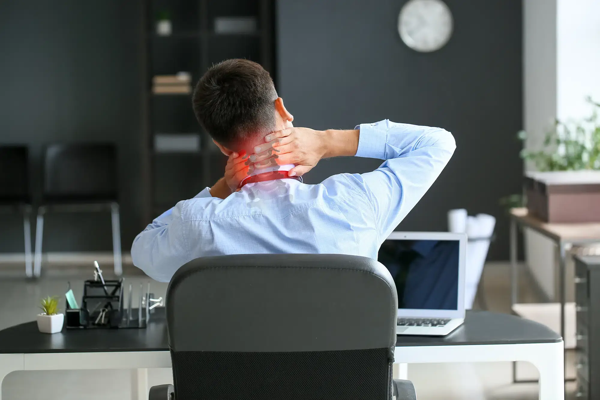 An office worker in Grand Rapids, MI, holds their neck in pain while sitting at a desk and working on a computer. This image illustrates the physical strain often associated with a sedentary work life in Kent County, Michigan.