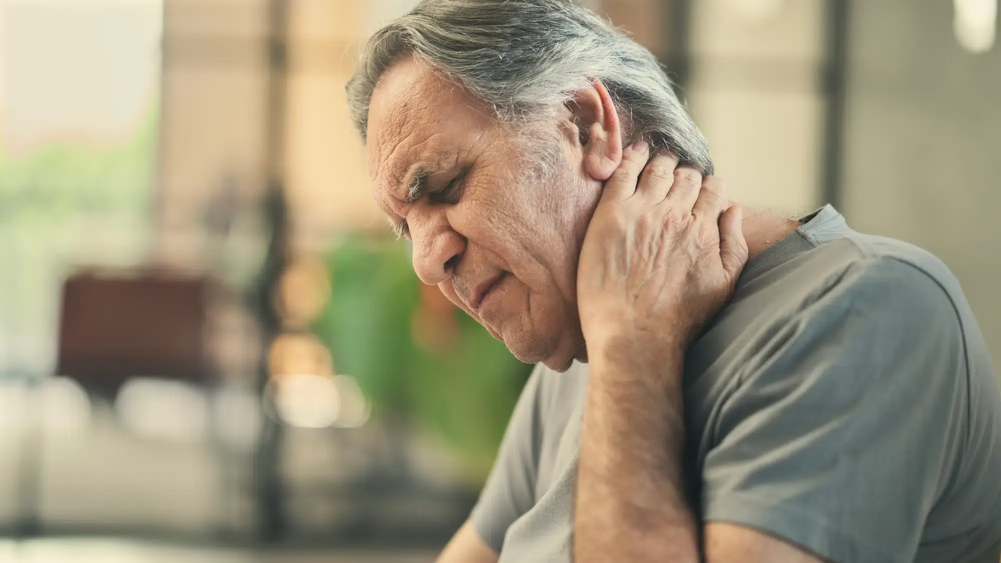 A man sits at his desk, wincing and holding his neck in pain while using his laptop. He may be suffering from neck pain and seeking chiropractic care for relief in Grand Rapids, MI.