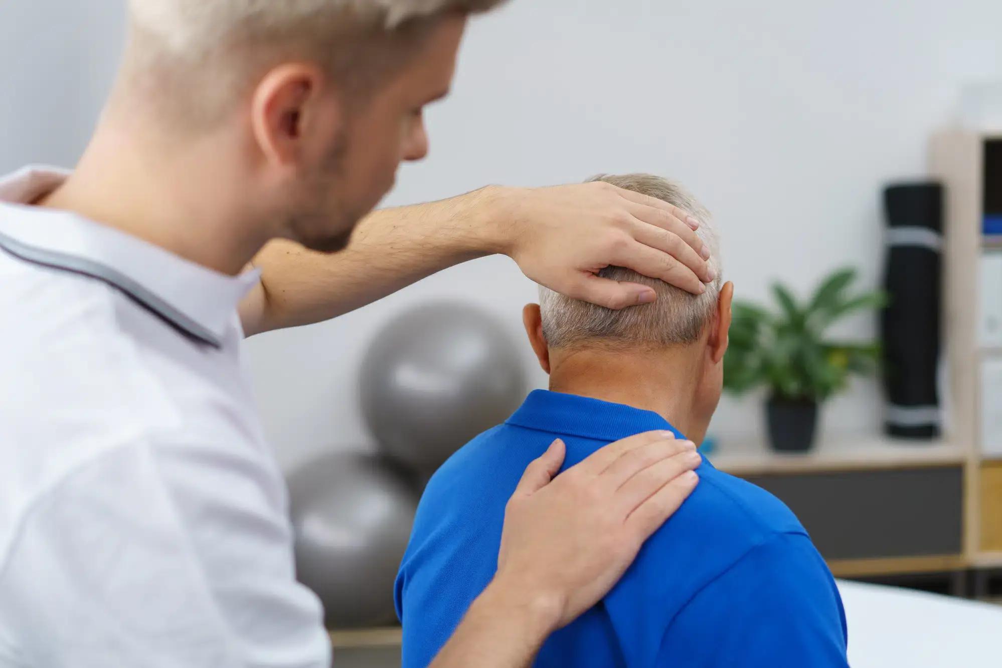 A physical therapist is gently stretching a patient's neck during a treatment session at a clinic in Grand Rapids, MI. The image shows a caring, professional interaction focused on patient recovery and wellness.