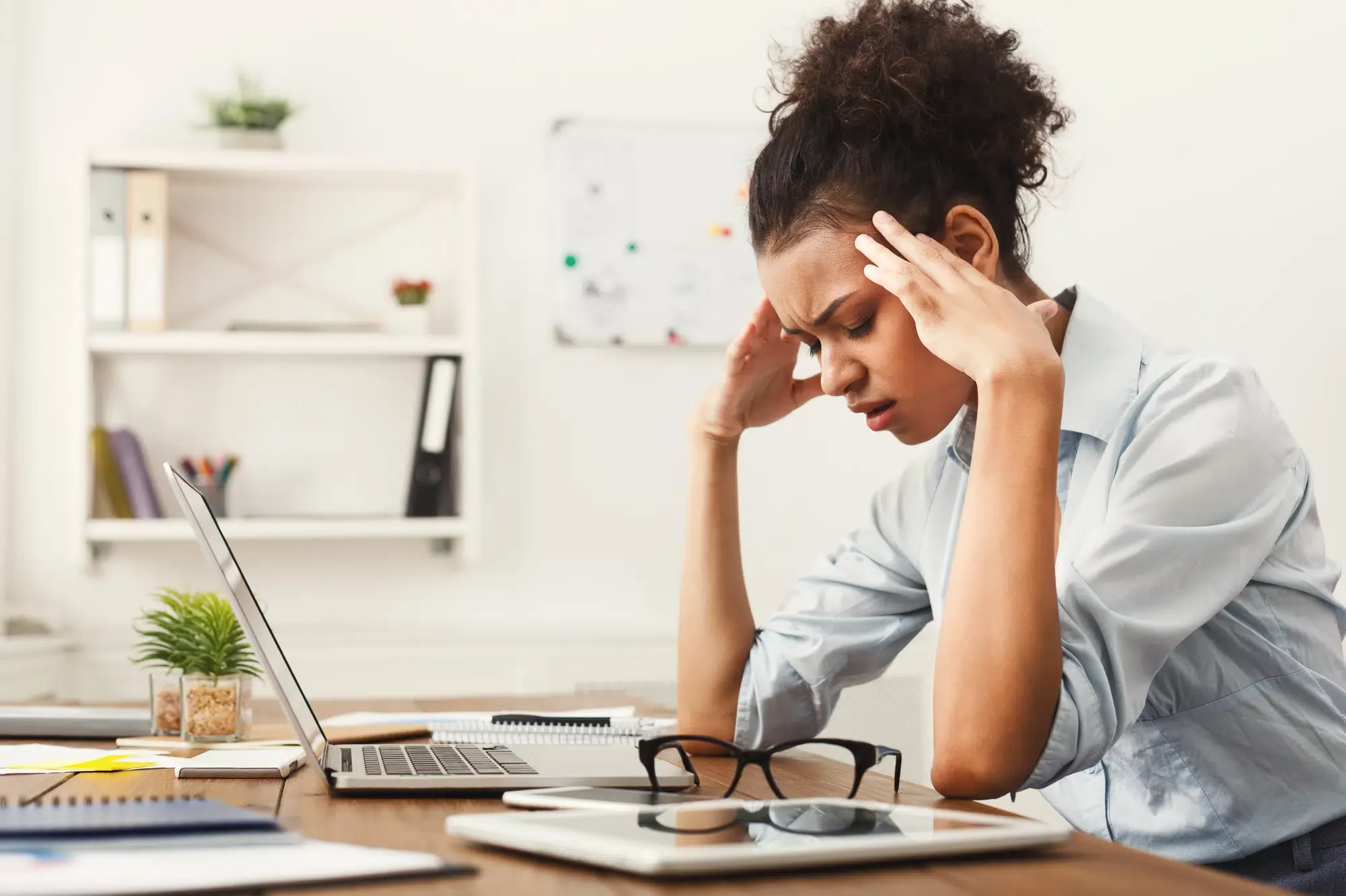 A woman sits at her desk, holding her head in pain while looking at her laptop. She appears to be suffering from a tension headache and may be seeking **headache pain relief in Grand Rapids, MI