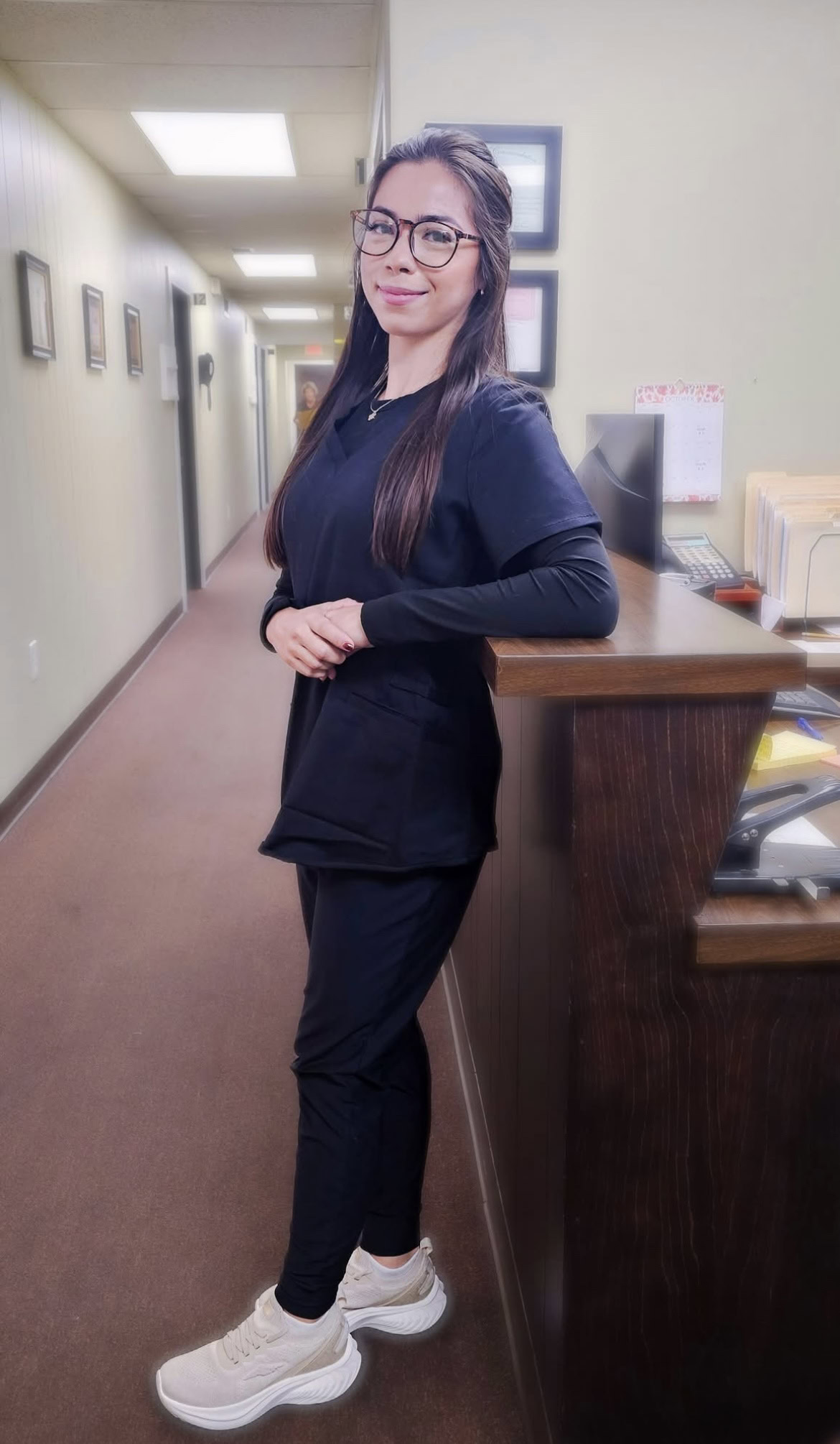 Chiropractic First staff member standing next to a wooden reception desk with a skeleton model in the background, emphasizing chiropractic care and holistic health services.